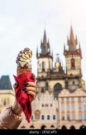Female hand is holding traditional czech cookie trdelnik on the old town background in Prague. Stock Photo