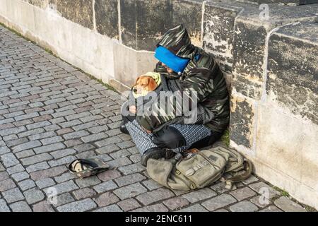 Prague, Czech Republic -January 20, 2020: omeless man with a dog sitting on the Charles bridge begging for help and money. Problems of big modern citi Stock Photo