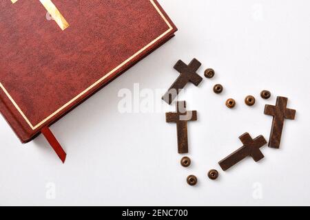 Background with bible and heart made with crosses and beads on white table. Horizontal composition. Top view Stock Photo