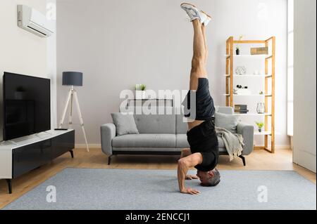Mature Man Doing Yoga Headstand Exercise Training At Home Stock Photo