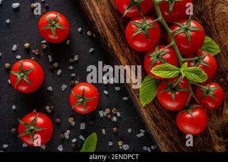 Fresh cherry tomatoes on a black background with spices. Food background. Top view. Stock Photo