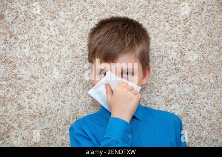 Boy with a cold virus wipes his nose from a runny nose