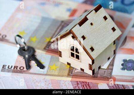 Wooden house model and keys on background of euro banknotes. Housing market, purchase or rental of real estate in Europe Stock Photo