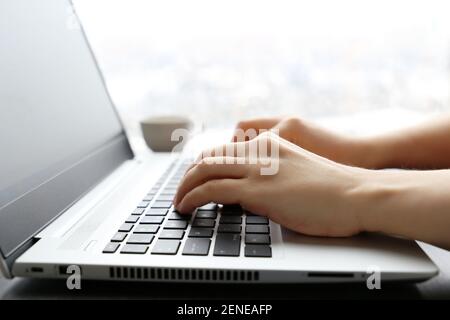 Woman works at laptop on window background. Female hands on keyboard in sunlight Stock Photo