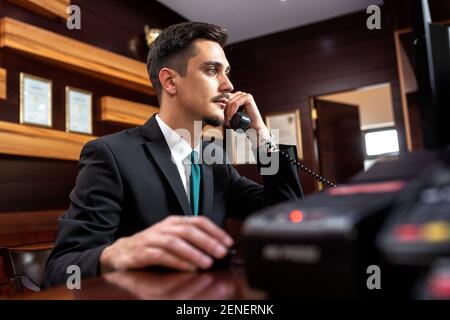 Smooth hotel reception worker talking on the phone, hotel operator Stock Photo