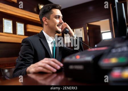 Smooth hotel reception worker talking on the phone, hotel operator Stock Photo