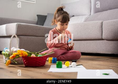 Baby girl painting Easter eggs at home. Stock Photo