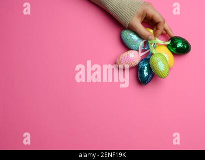 female hand holding multicolored decorative easter eggs on pink background, copy space Stock Photo