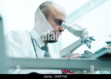 young scientist studying fluid samples through a microscope . Stock Photo