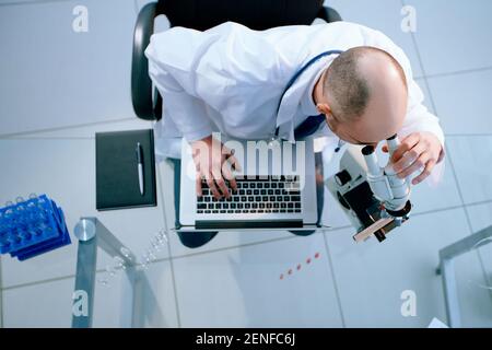 scientist looking through a microscope and using a laptop during his research. Stock Photo
