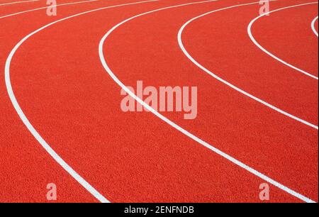 Curved white lines on a bright red artificial running track create an abstract and random image. Stock Photo