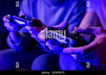 friends playing console video games. controller in hands closeup. neon lights Stock Photo