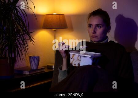 lonely sad woman eating ice cream from container while sitting on couch and watching tv at home Stock Photo