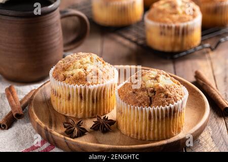 Two cinnamon muffins on a wooden plate with cup of coffee and muffins on a rack in background Stock Photo