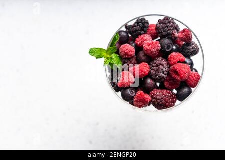 frozen blueberries, raspberries and blackberries on a light textured background. in a tall transparent cocktail glass. copyspace Stock Photo