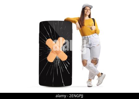 Full length portrait of a female student leaning on a phone with cracked screen and bandage and pointing isolated on white background Stock Photo