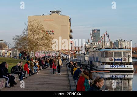 Vorfruehling in Berlin Mitte Februar 2021 , Spreeufer bei der East Side Gallery , Spaziergaenger, Promenade, Hostel Boat, Stock Photo