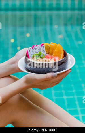Woman holding smoothie bowl and fruits by swimming pool. Stock Photo