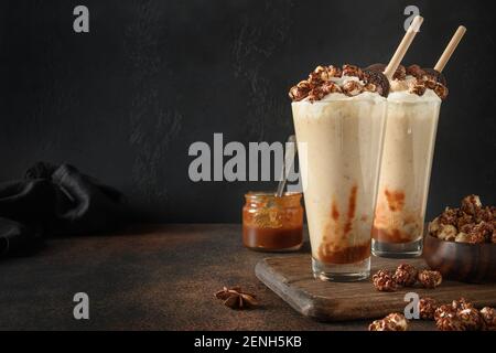 Tasty banana and caramel milkshake garnished whipped cream and popcorn on dark brown background. Stock Photo