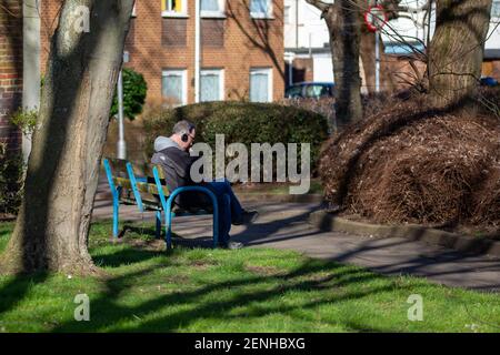 A man sitting on a bench in the park reading and listening to music Stock Photo