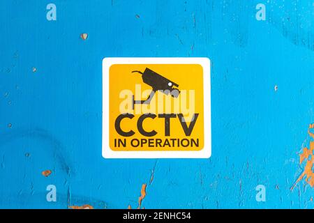 A CCTV in operation sign on a blue wooden door with flaking paint Stock Photo