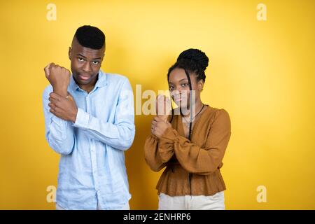 Young african american couple standing over yellow background suffering pain on hands and fingers, arthritis inflammation Stock Photo