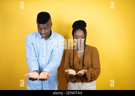 Young african american couple standing over yellow background Smiling with hands palms together receiving or giving gesture. Hold and protection Stock Photo