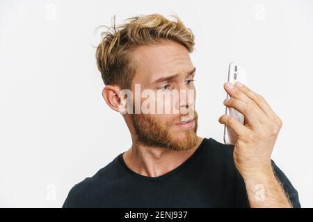 Confused caucasian blonde man using mobile phone isolated over white background Stock Photo