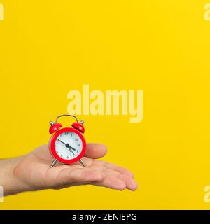 Time management concept. Hand with small red alarm clock on trendy yellow color background Stock Photo