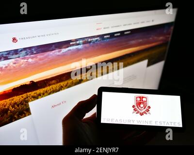Person holding smartphone with logo of Australian winemaking company Treasury Wine Estates on screen in front of website. Focus on phone display. Stock Photo