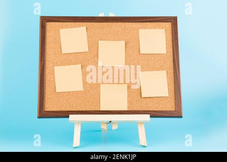Wooden easel with cork boardand paper stickers on blue background. Stock Photo