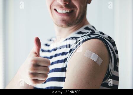 Happy young man showing thumb up and his arm after vaccination. Themes prevention, vaccine and health care during pandemic covid-19. Stock Photo