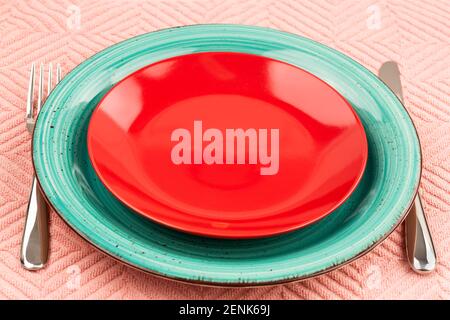 Two colorful empty plates with knife and fork on pink cotton towel. Stock Photo