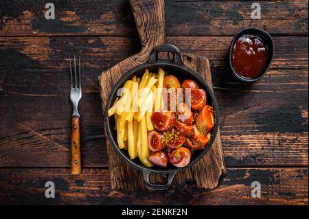 Currywurst street food meal, Curry spice on wursts served French fries in a pan. Dark wooden background. Top view Stock Photo