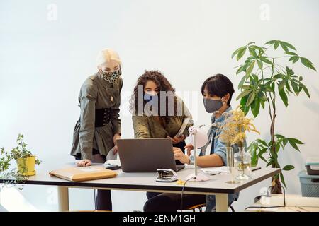 Colleagues looking at laptop, wearing face masks Stock Photo