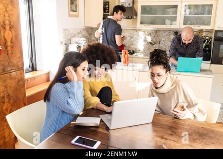 Housemates in kitchen, using laptops, having video Stock Photo