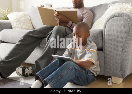 Boy sitting on floor using digital tablet, father Stock Photo