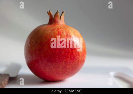 A single pomegranate in closeup on a white chopping board and background with a knife Stock Photo