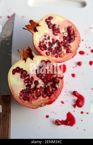 Closeup of a single pomegranate cut open into slices on a white chopping board with with juicy pips Stock Photo