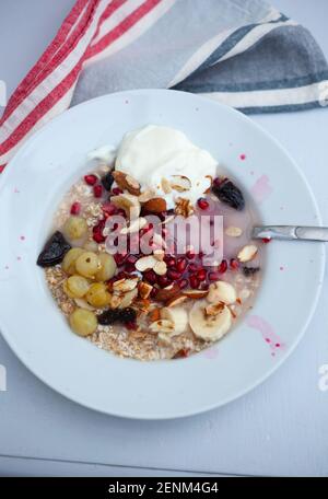 Bowl of meusli, nuts and fruit including pomegranates, banana slices,fat free yoghurt and gooseberries Stock Photo