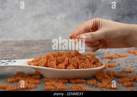 Female hand picking raw macaroni from plate on marble background Stock Photo