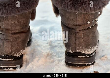 Women's winter boots on snow. Brown warm fluffy winter shoes close-up. Stock Photo