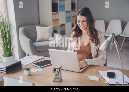 Photo portrait of pregnant woman sitting working on laptop at desk in modern office Stock Photo