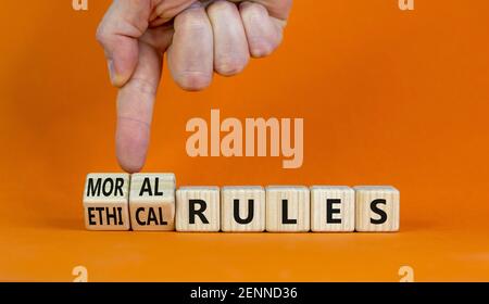 Ethical or moral rules symbol. Businessman turns wooden cubes and changes words 'ethical rules' to 'moral rules' on a beautiful orange background. Bus Stock Photo