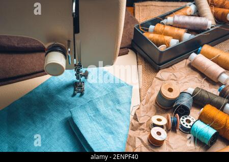 Thread, scissors, and fabric against a blurry sewing machine. Top view. Stock Photo