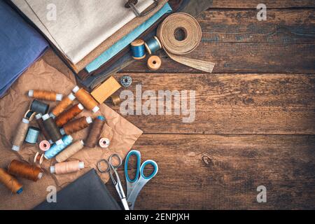 Threads and fabrics of different colors, scissors and a thimble with a ribbon on a wooden background. Stock Photo
