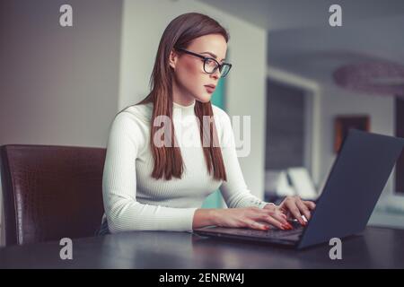 Young smart Caucasian woman in eyeglasses working on laptop at home Stock Photo