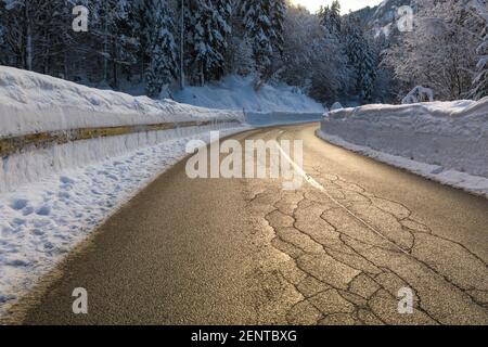 Driving on a snowy winter road through a forest in nature with sun shining. Stock Photo