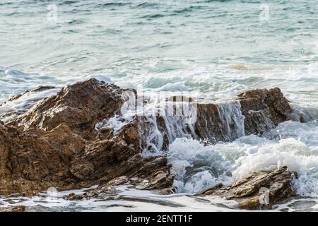 closeup of wave gently flowing over rock on california coastline; water cascading down the side. Pacific ocean in the background. Stock Photo