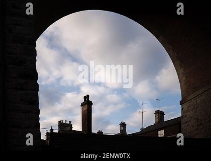 Tall old chimney pots tops under railway bridge arches on homes and houses below red brick train arch silhouetted on summer day in sunshine Mansfield Stock Photo